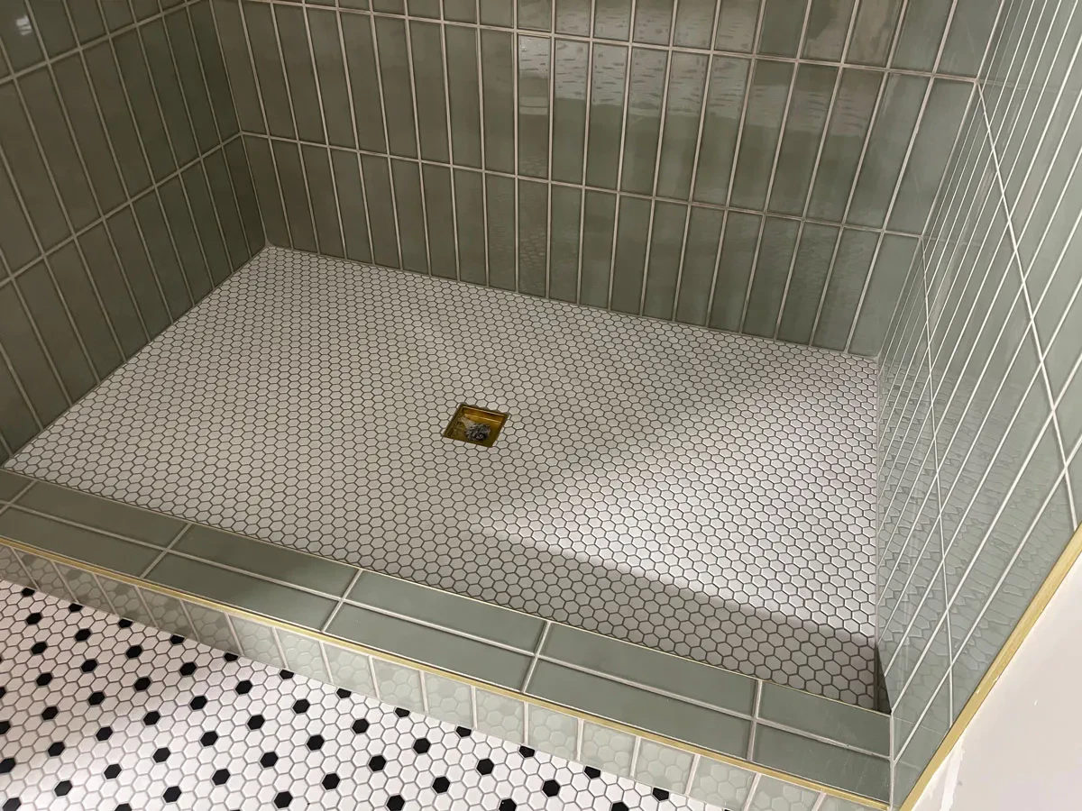 Green-tiled walk-in shower with hexagonal floor tiles.